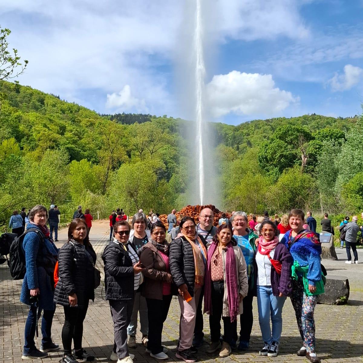 Gruppenfoto vor der Fontäne des Geysirs, im Hintergrund ein grüner Hügel.