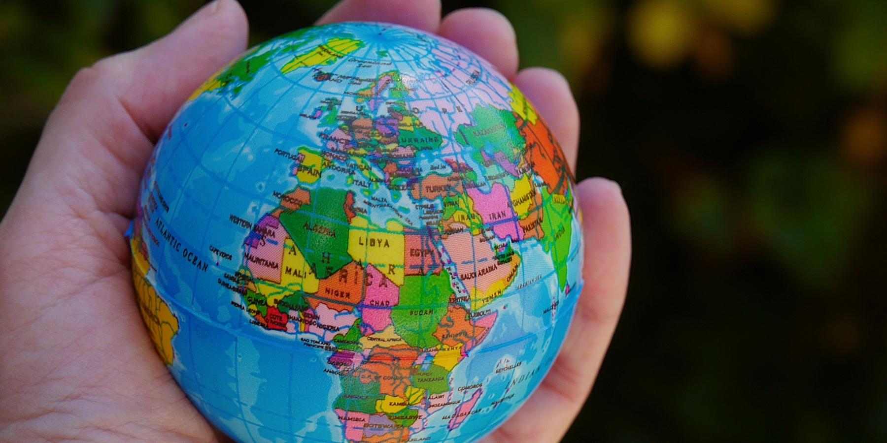 Eine Hand hält einen Ball, der auf der Oberfläche die Weltkugel zeigt, im Vordergrund Afrika und Europa.