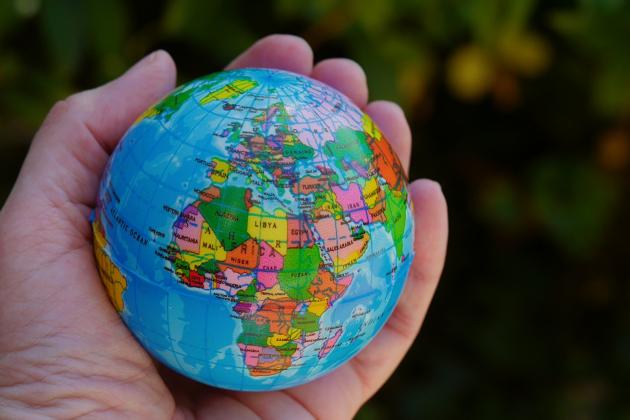 Eine Hand hält einen Ball, der auf der Oberfläche die Weltkugel zeigt, im Vordergrund Afrika und Europa.