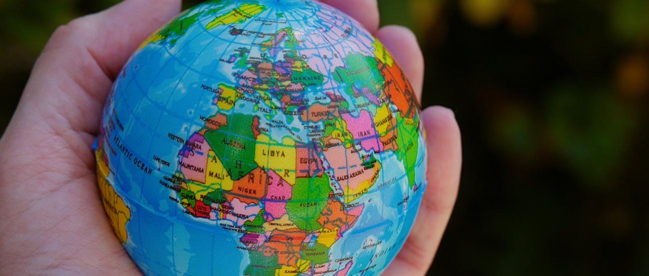 Eine Hand hält einen Ball, der auf der Oberfläche die Weltkugel zeigt, im Vordergrund Afrika und Europa.