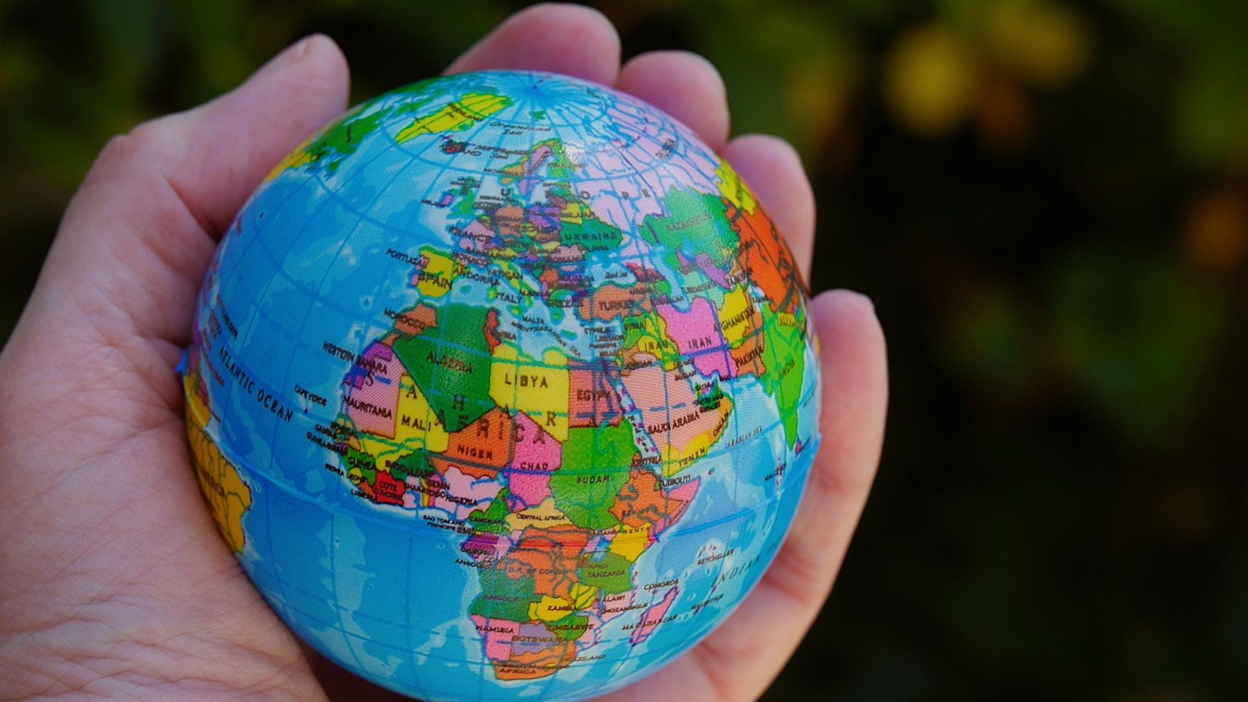 Eine Hand hält einen Ball, der auf der Oberfläche die Weltkugel zeigt, im Vordergrund Afrika und Europa.