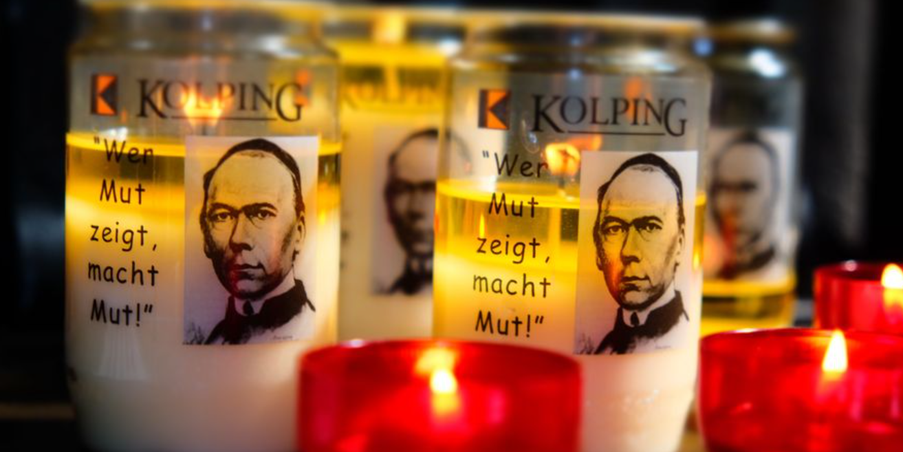 Kolpingkerzen (c) KOLPING INTERNATIONAL Das Bild zeigt entzündete Kerzen in roten Haltern im Vordergrund, dahinter Öllichter mit dem Portrait Adolph Kolpings.