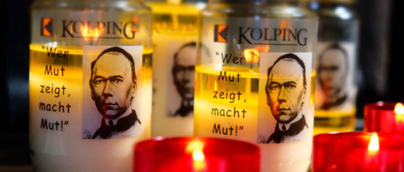 Das Bild zeigt entzündete Kerzen in roten Haltern im Vordergrund, dahinter Öllichter mit dem Portrait Adolph Kolpings.