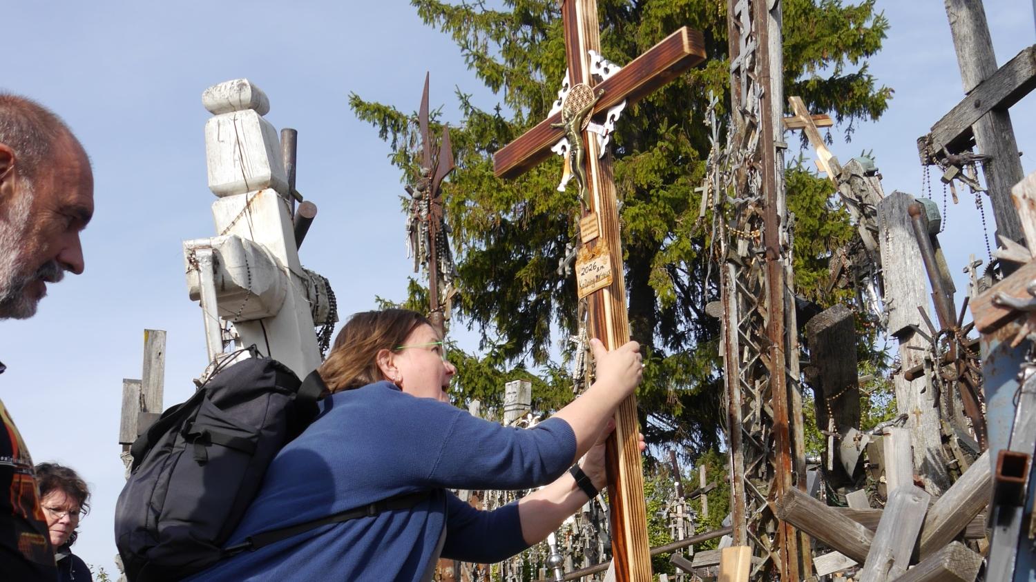 Das Bild zeigt drei Menschen, die ein neues Kreuz inmitten vieler anderer Kreuze aufstellen.