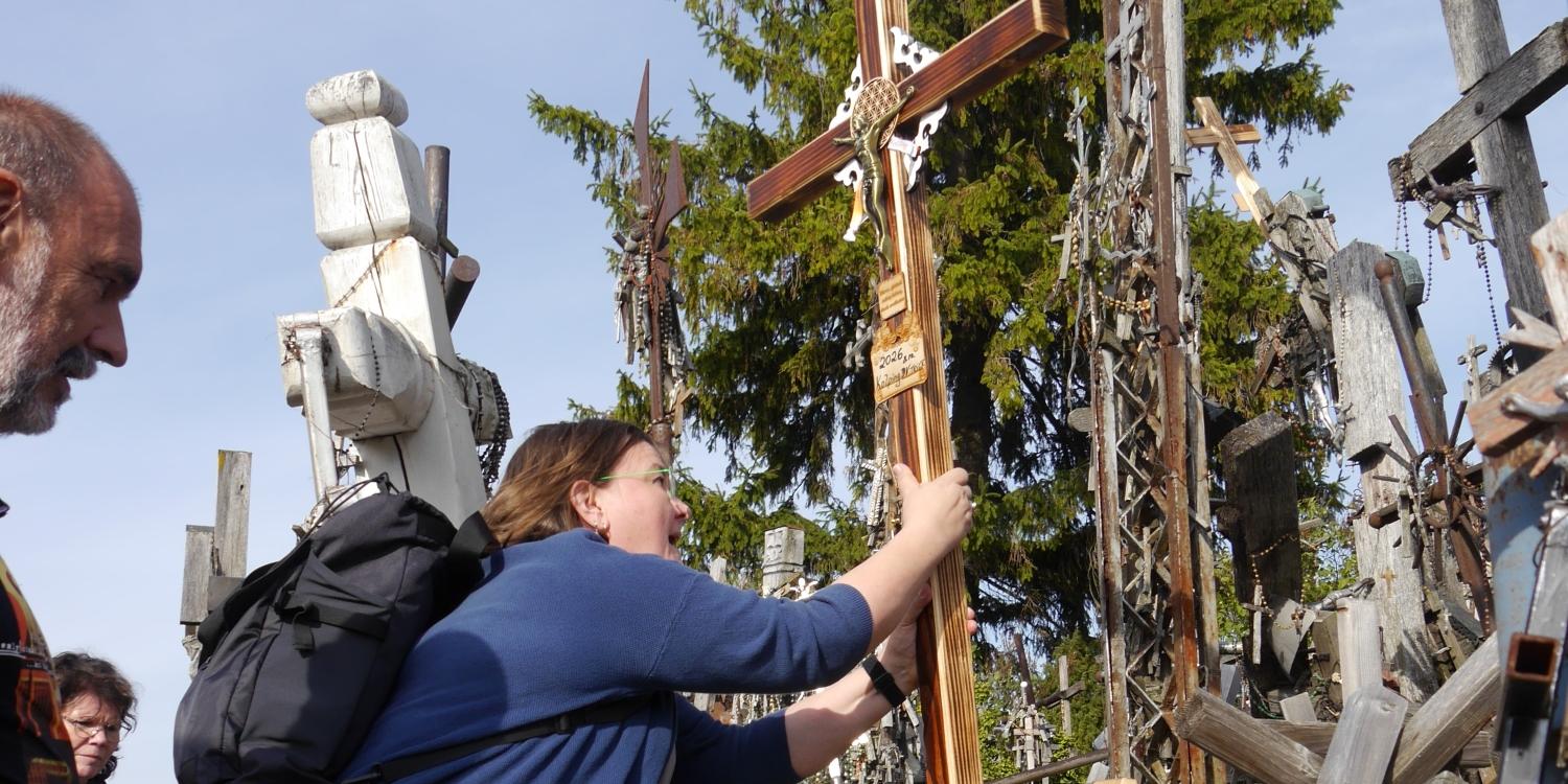Das Bild zeigt drei Menschen, die ein neues Kreuz inmitten vieler anderer Kreuze aufstellen.