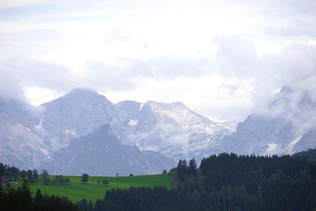 Das Bild zeigt eine Berglandschaft mit grünen Hügeln im Vordergrund und Felsmassiv im Hintergrund.