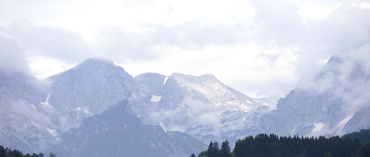 Das Bild zeigt eine Berglandschaft mit grünen Hügeln im Vordergrund und Felsmassiv im Hintergrund.