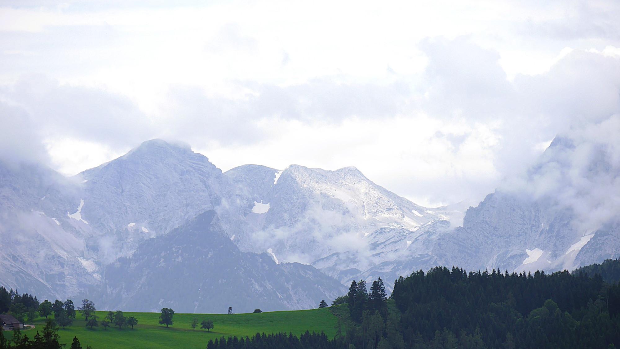Das Bild zeigt eine Berglandschaft mit grünen Hügeln im Vordergrund und Felsmassiv im Hintergrund.