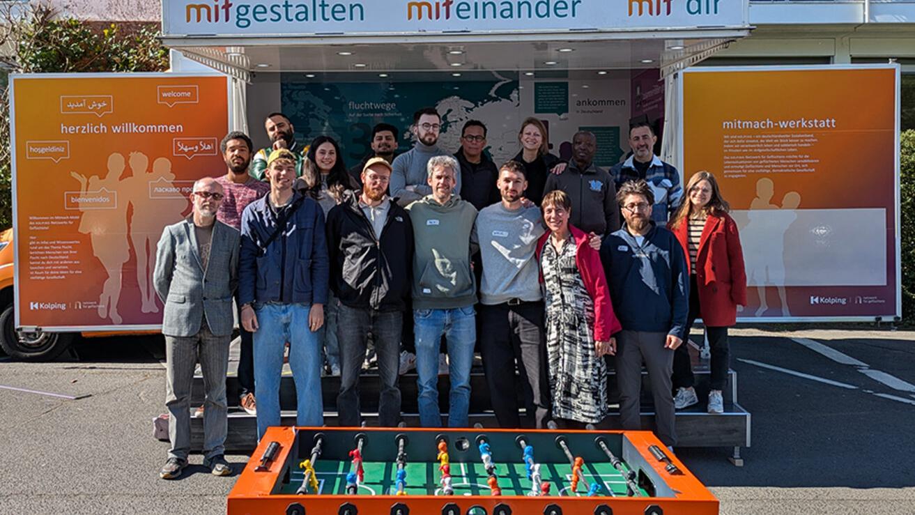 Eine Gruppe von Menschen steht vor dem Mitmachmobil des Kolping-Netzwerkes für Geflüchtete.