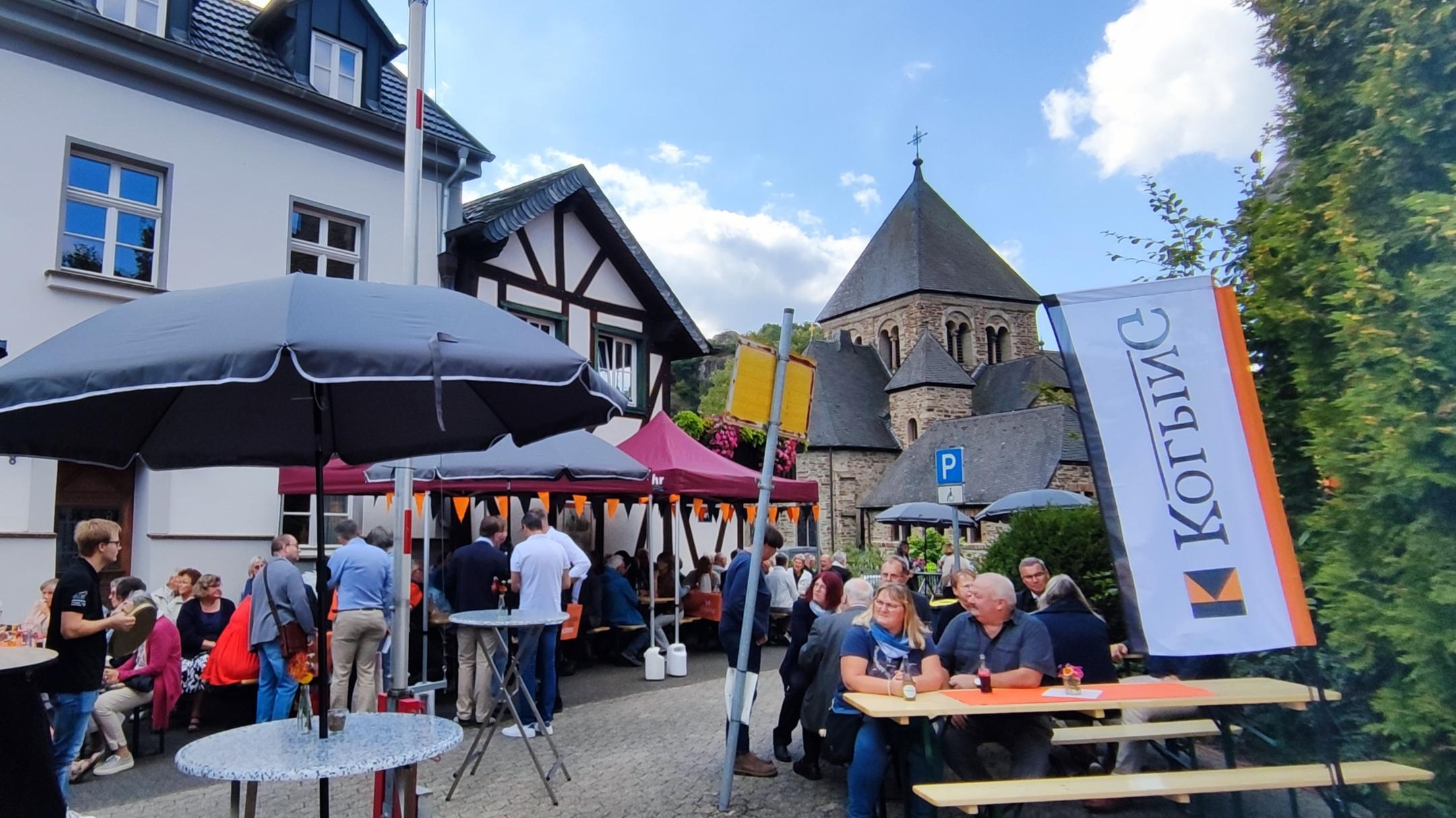 Dorfplatz mit Biertischen und Menschen, die fröhlich feiern.