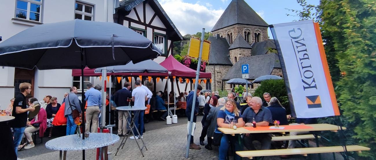Dorfplatz mit Biertischen und Menschen, die fröhlich feiern.