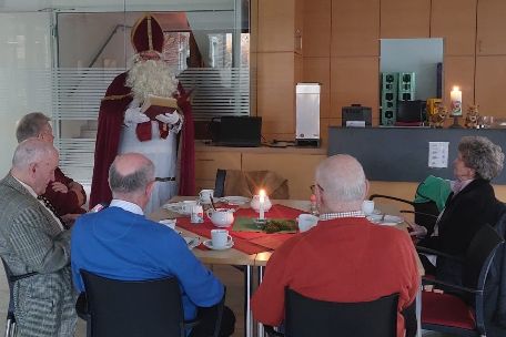 Menschen sitzen am Tisch und hören dem Nikolaus zu