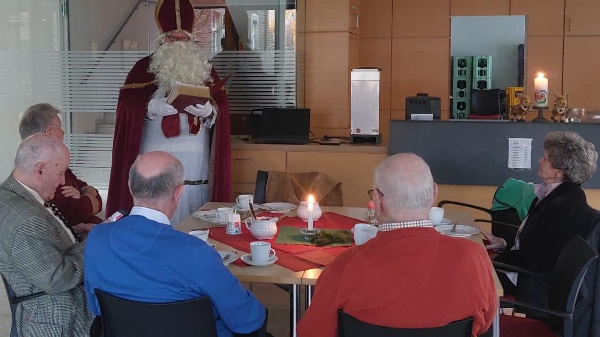 Menschen sitzen am Tisch und hören dem Nikolaus zu