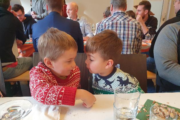 im Vordergrund zwei Kinder in Weihnachtspullis, im Hintergrund Menschen im Gespräch