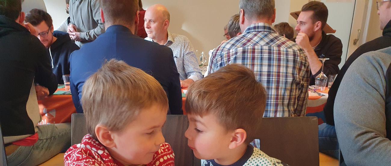 im Vordergrund zwei Kinder in Weihnachtspullis, im Hintergrund Menschen im Gespräch