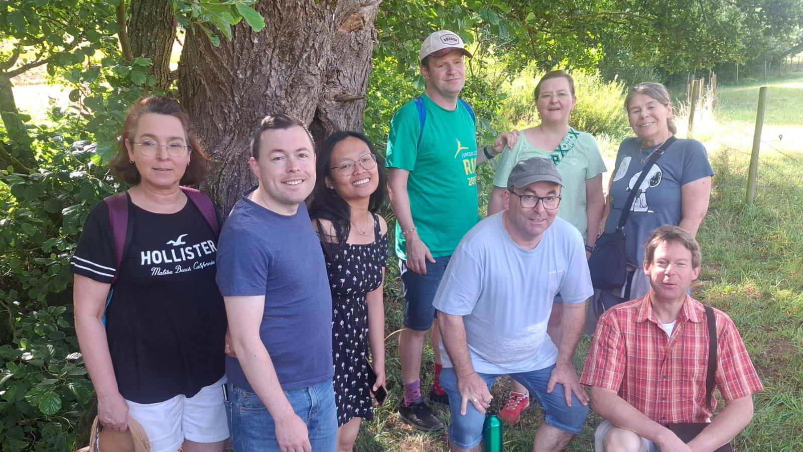 Wandergruppe steht unter einem schattigen Baum auf einer Wiese