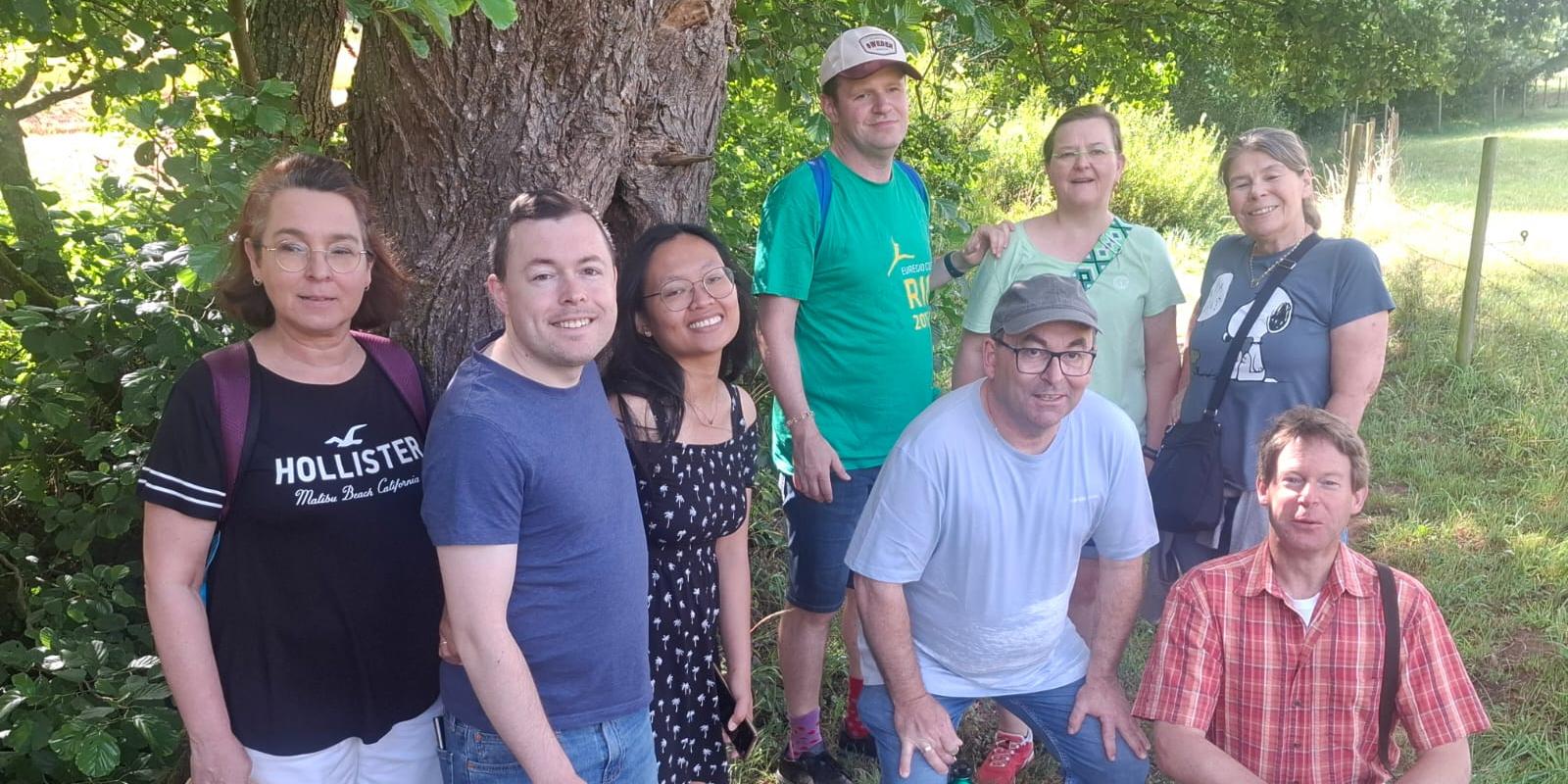 Wandergruppe steht unter einem schattigen Baum auf einer Wiese