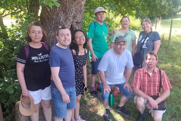 Wandergruppe steht unter einem schattigen Baum auf einer Wiese