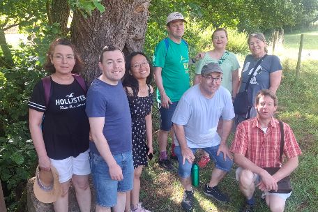 Wandergruppe steht unter einem schattigen Baum auf einer Wiese