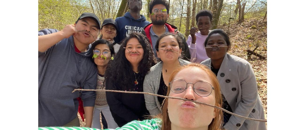 Junge Menschen posieren fröhlich für ein Selfie und balancieren dabei einen Zweig zwischen Oberlippe und Nase.