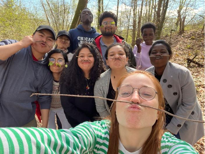 Junge Menschen posieren fröhlich für ein Selfie und balancieren dabei einen Zweig zwischen Oberlippe und Nase.
