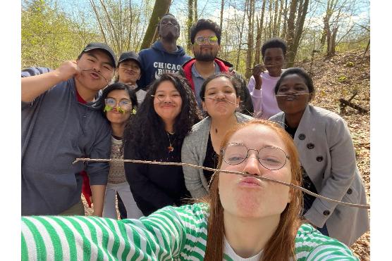 Junge Menschen posieren fröhlich für ein Selfie und balancieren dabei einen Zweig zwischen Oberlippe und Nase.