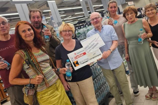 in einem Getränkemarkt stehen vor Getränkekisten 8 Personen - eine Person überreicht einen symbolischen Scheck