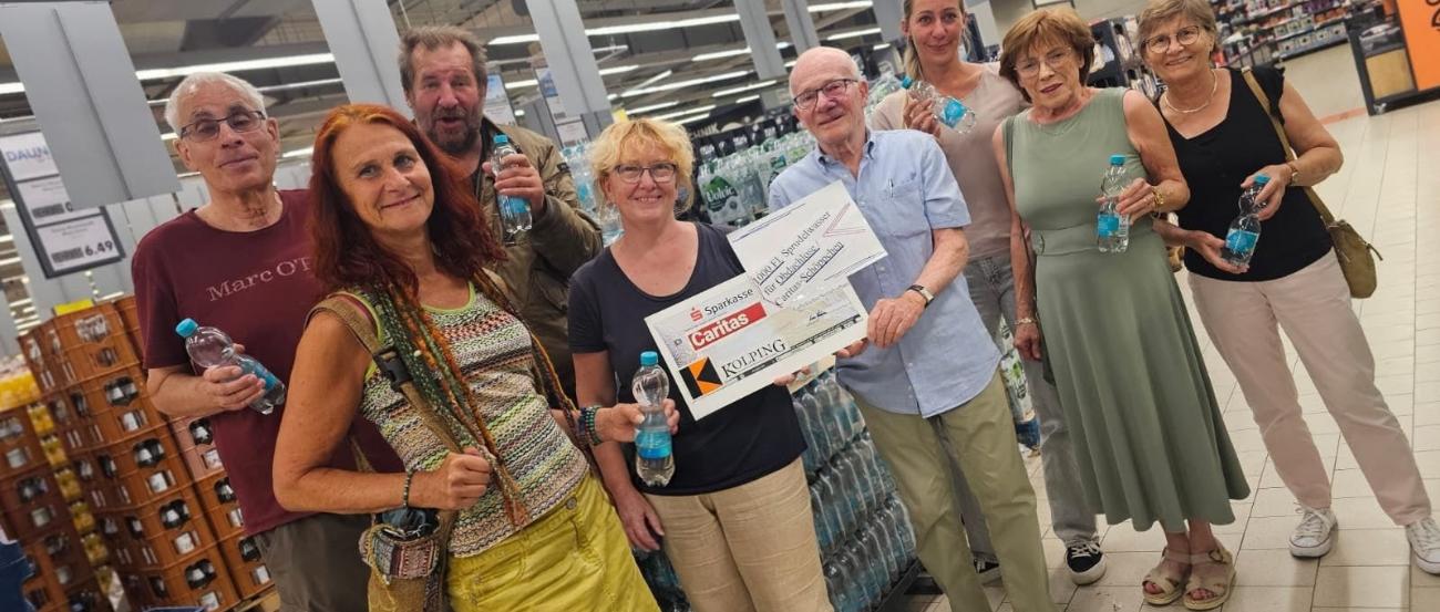 in einem Getränkemarkt stehen vor Getränkekisten 8 Personen - eine Person überreicht einen symbolischen Scheck