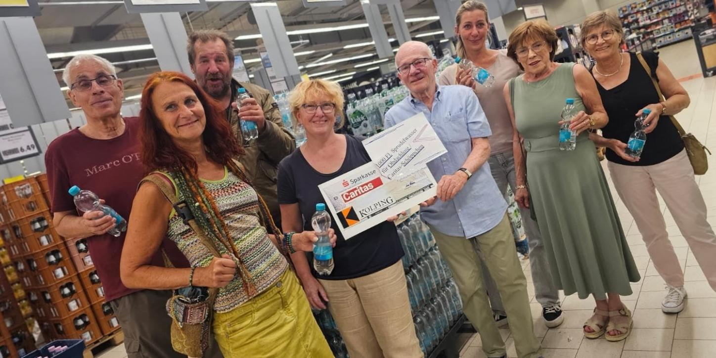 in einem Getränkemarkt stehen vor Getränkekisten 8 Personen - eine Person überreicht einen symbolischen Scheck