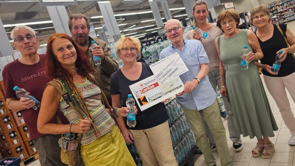 in einem Getränkemarkt stehen vor Getränkekisten 8 Personen - eine Person überreicht einen symbolischen Scheck