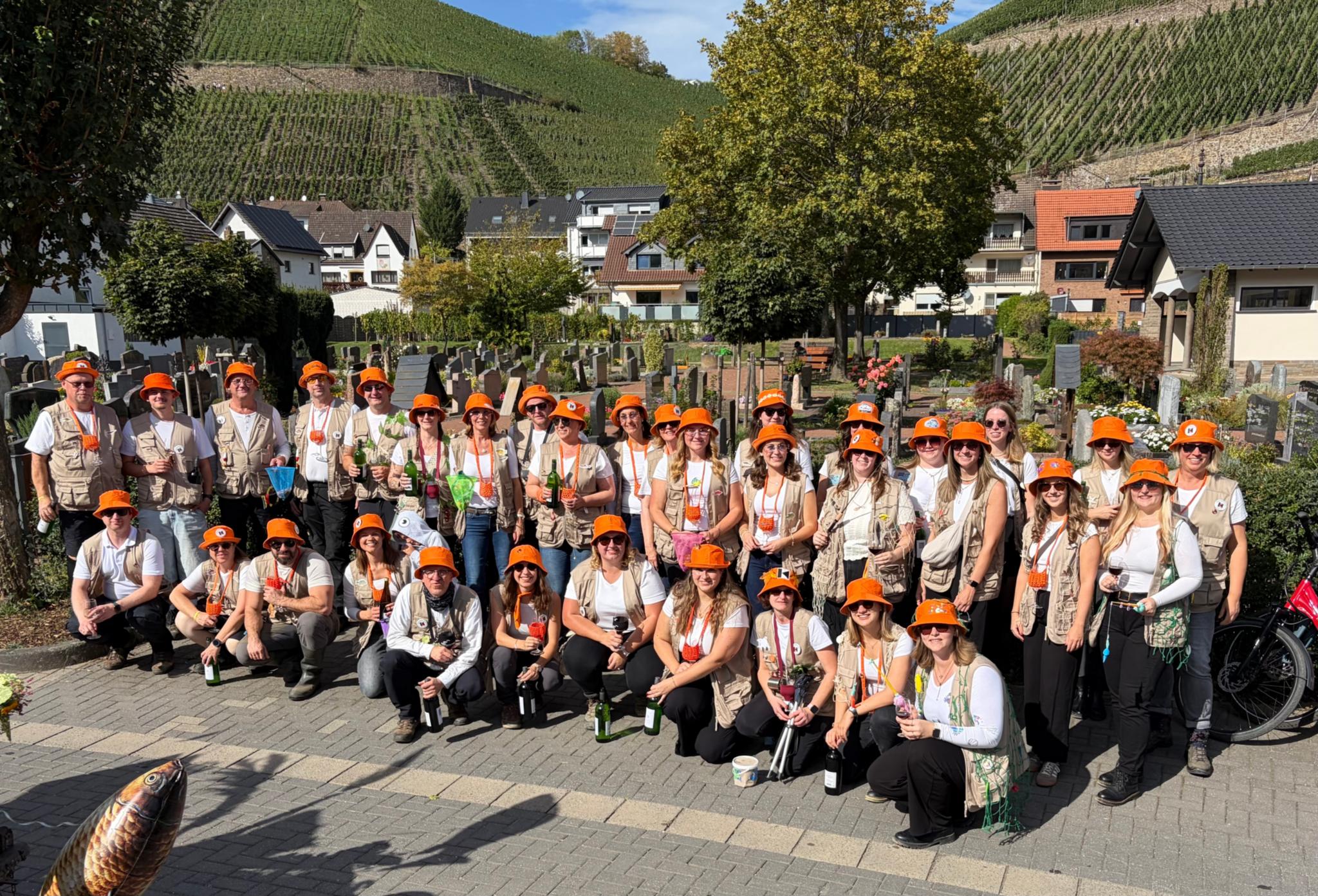 Gruppenbild Dernau Winzerfest 2026 (c) Kolpingsfamilie Dernau Gruppenbild mit allen Zugteilnehmern mit orangenem Fischerhut, im Hintergrund Dernau und Weinberge