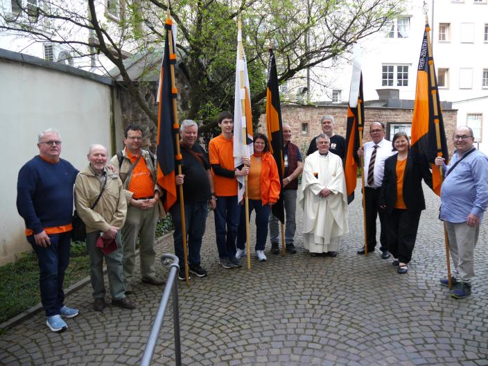 Menschen stehen im Halbkreis im Hof der St. Gangolf-Kirche, einige halten Kolpingbanner.