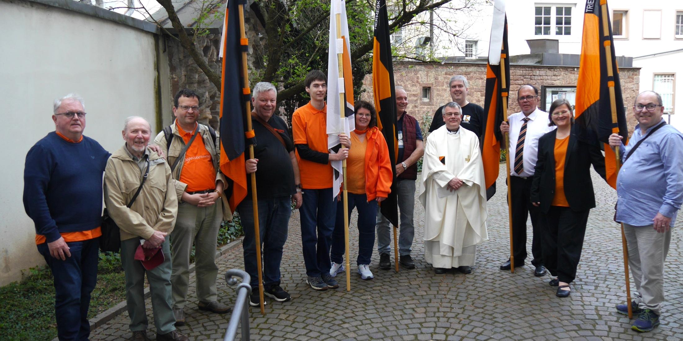 Menschen stehen im Halbkreis im Hof der St. Gangolf-Kirche, einige halten Kolpingbanner.
