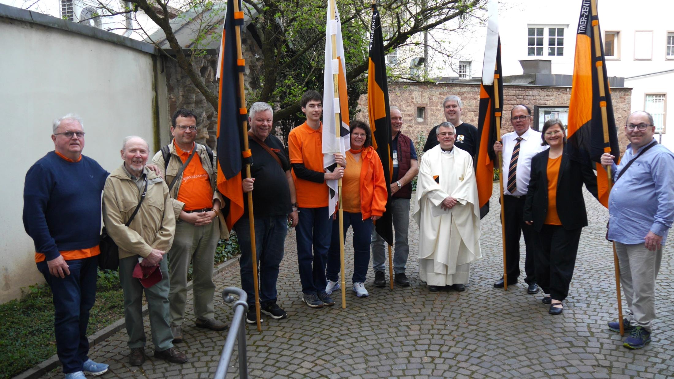 Menschen stehen im Halbkreis im Hof der St. Gangolf-Kirche, einige halten Kolpingbanner.