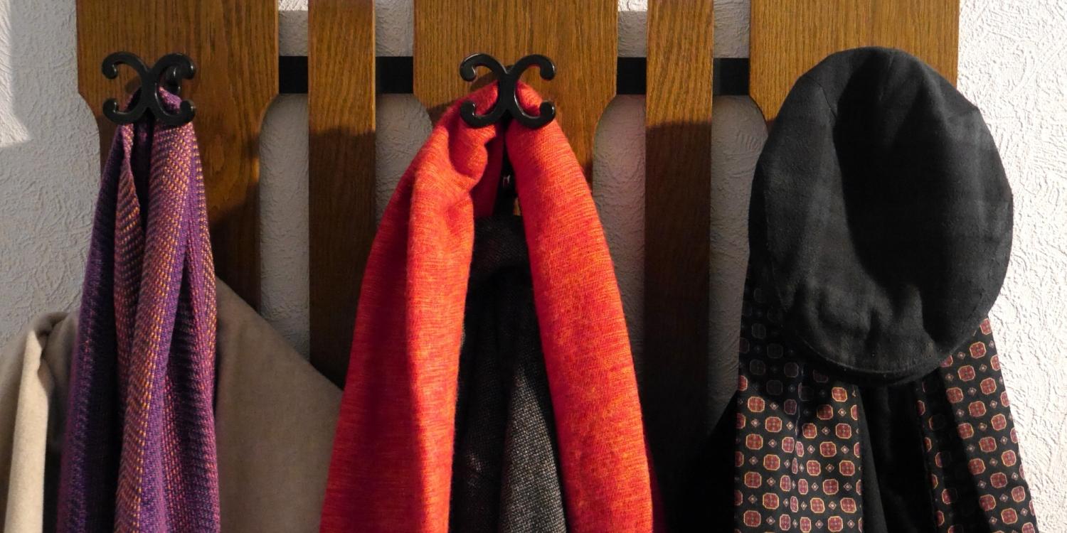 An einer Garderobe hängen drei Wintermäntel mit jeweils einem Schal sowie eine Kappe.