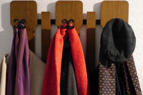 An einer Garderobe hängen drei Wintermäntel mit jeweils einem Schal sowie eine Kappe.