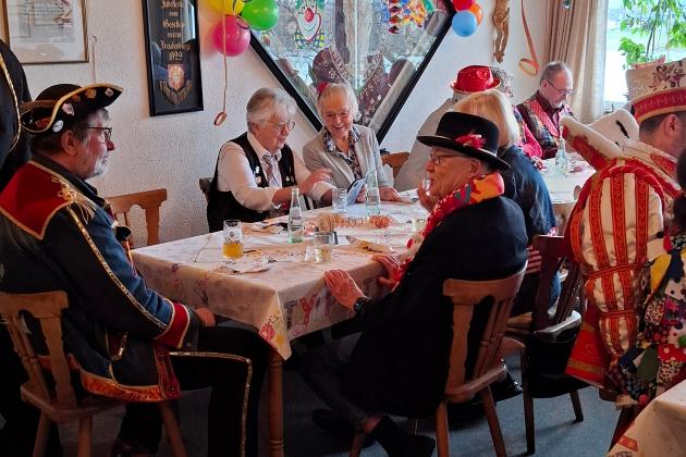 ein karnevalistisch geschmückter Raum, am Tisch sitzen verkleidete Menschen