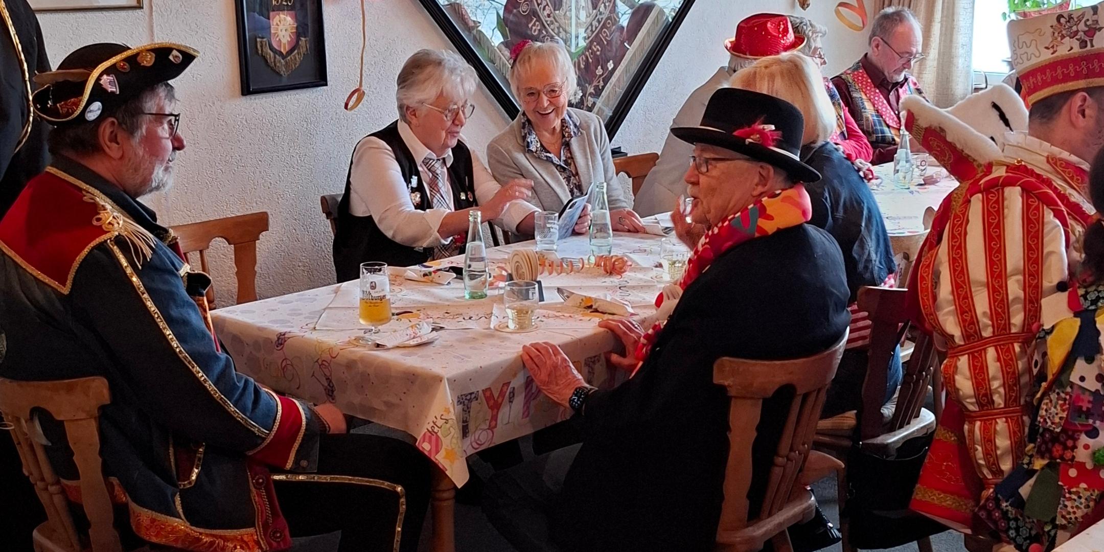 ein karnevalistisch geschmückter Raum, am Tisch sitzen verkleidete Menschen