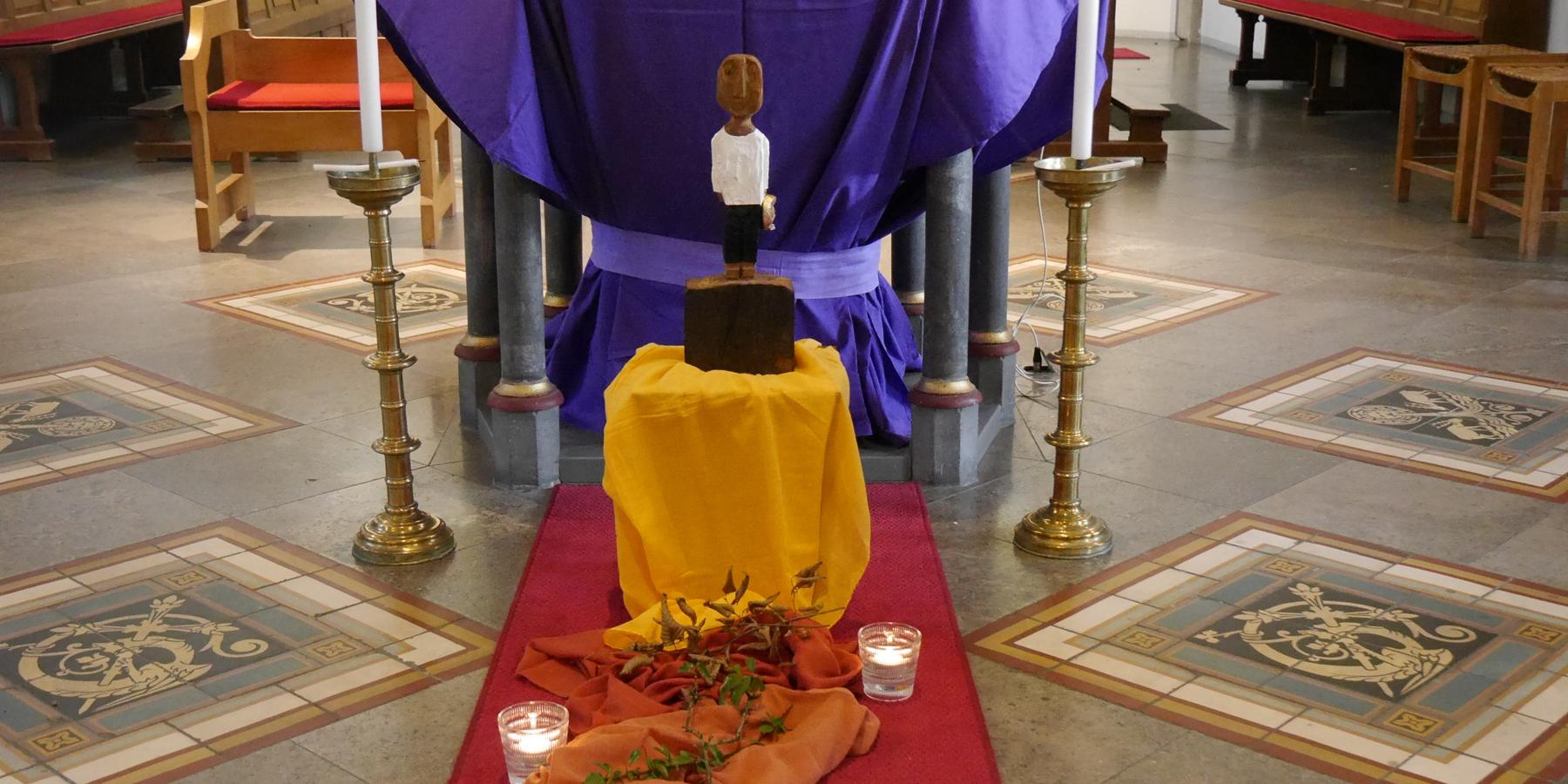 Vor einem Altar steht eine Königsskulptur, davor ein Weg aus Tüchern gelegt mit Steinen, Dornen und welkem Laub darauf, daneben drei Kerzen. (c) Martina Wagner Vor einem Altar steht eine Königsskulptur, davor ein Weg aus Tüchern gelegt mit Steinen, Dornen und welkem Laub darauf, daneben drei Kerzen.