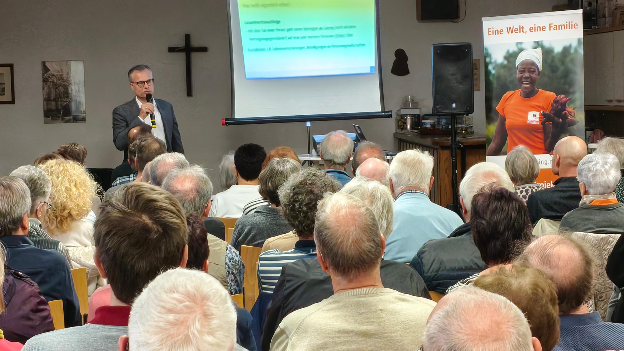 Das Bild zur Infoveranstaltung zeigt das Publikum von hinten, vorne steht der Referent neben einer Leinwand.