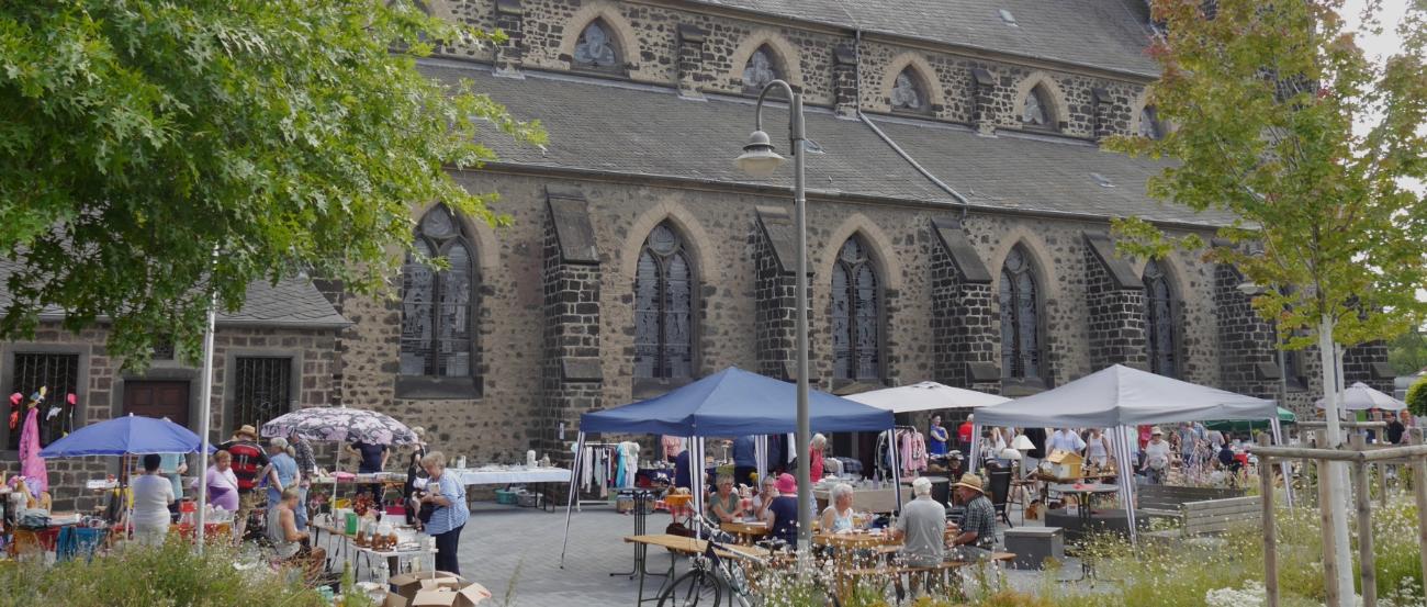 Auf dem Platz neben einer Kirche stehen Tische und Pavillons des Flohmarkts.