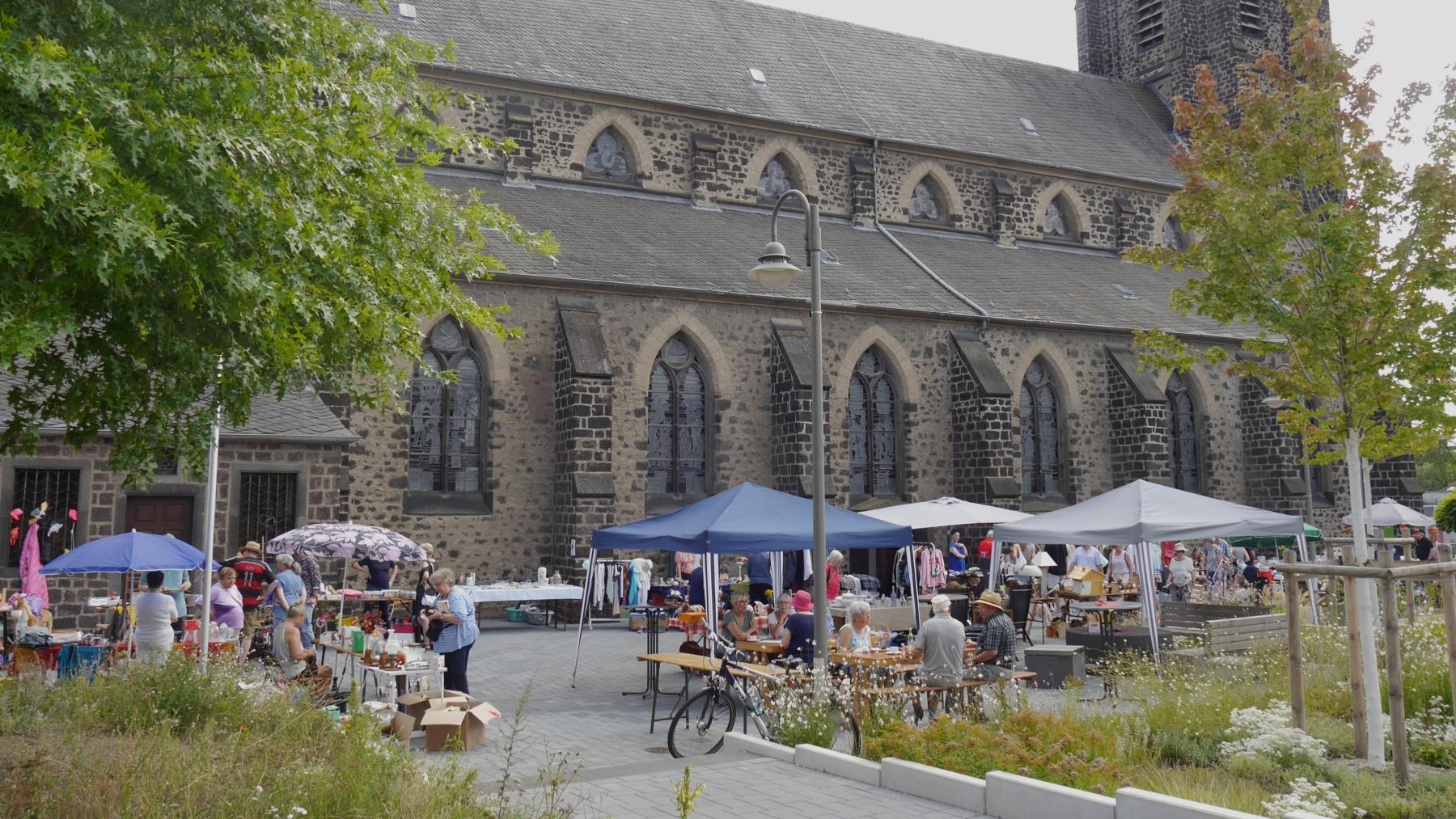Auf dem Platz neben einer Kirche stehen Tische und Pavillons des Flohmarkts.