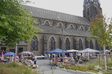 Auf dem Platz neben einer Kirche stehen Tische und Pavillons des Flohmarkts.