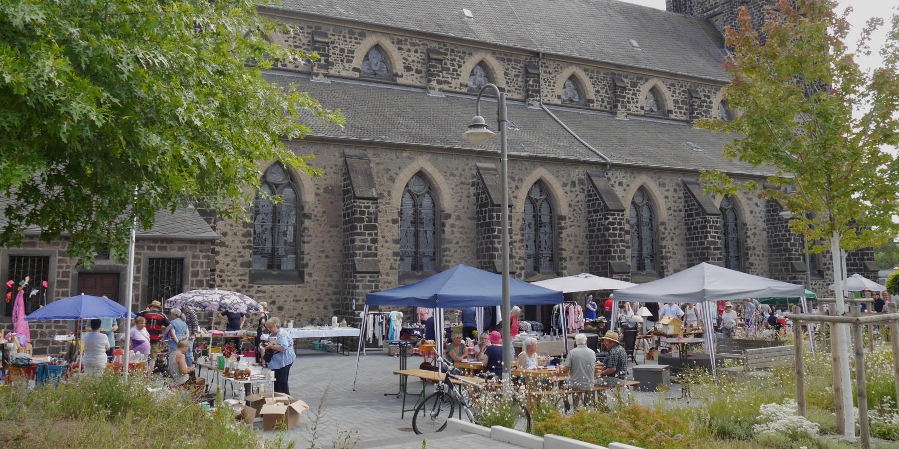 Auf dem Platz neben einer Kirche stehen Tische und Pavillons des Flohmarkts.