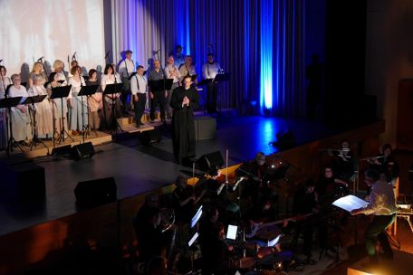 Auf einer Bühne im Scheinwerferlicht ist ein Chor und ein Darsteller in der Rolle des Adolph Kolping zu sehen, vor der Bühne ist ein Orchester.