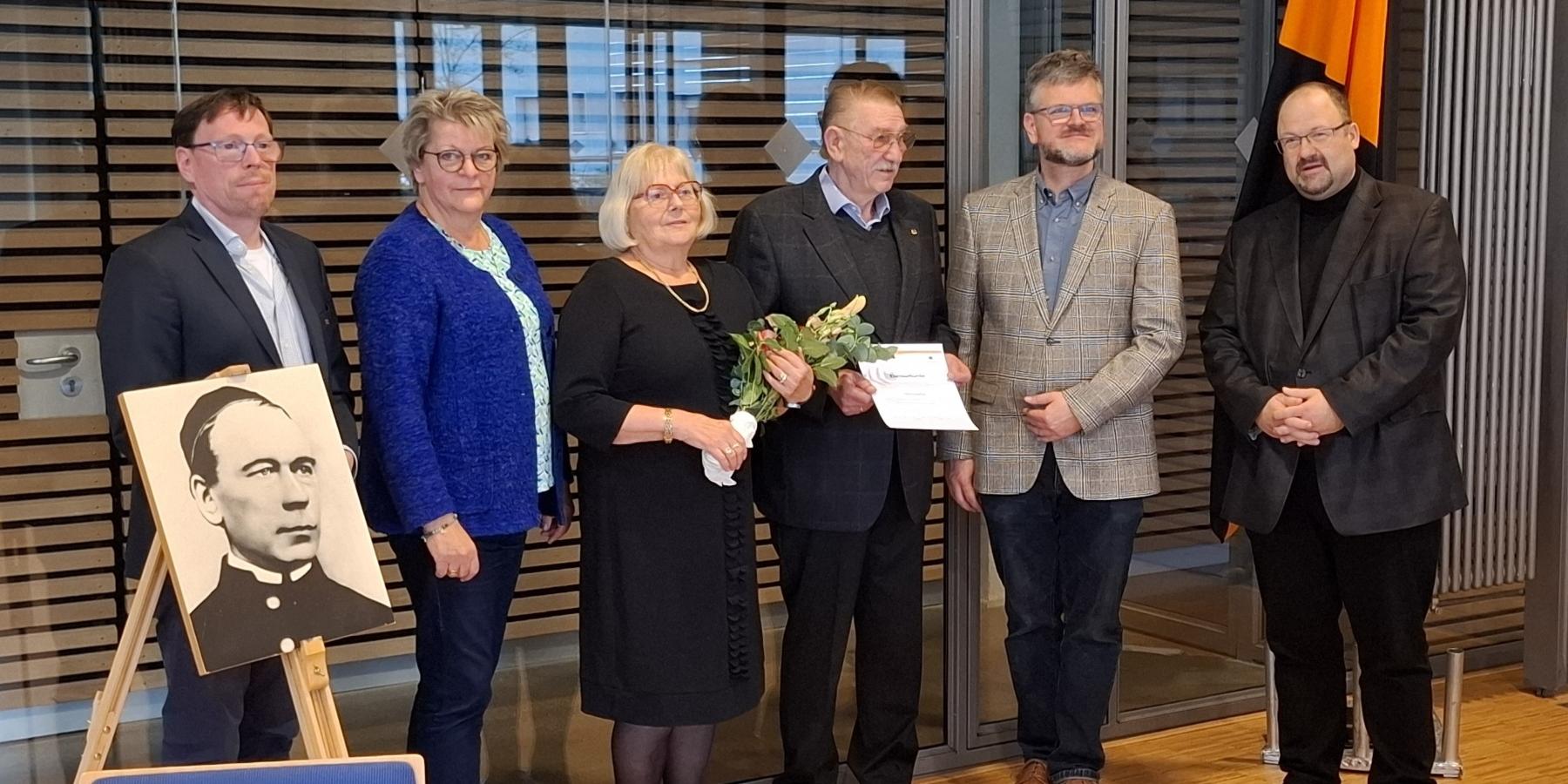 Ehrung des langjährigen Vorsitzenden mit Ehefrau durch das neue Leitungsteam und den Präses, die Personen stehen neben einem Bild von Adolph Kolping. (c) Kolpingsfamilie Andernach Ehrung des langjährigen Vorsitzenden mit Ehefrau durch das neue Leitungsteam und den Präses, die Personen stehen neben einem Bild von Adolph Kolping.