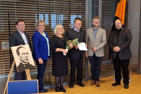 Ehrung des langjährigen Vorsitzenden mit Ehefrau durch das neue Leitungsteam und den Präses, die Personen stehen neben einem Bild von Adolph Kolping.