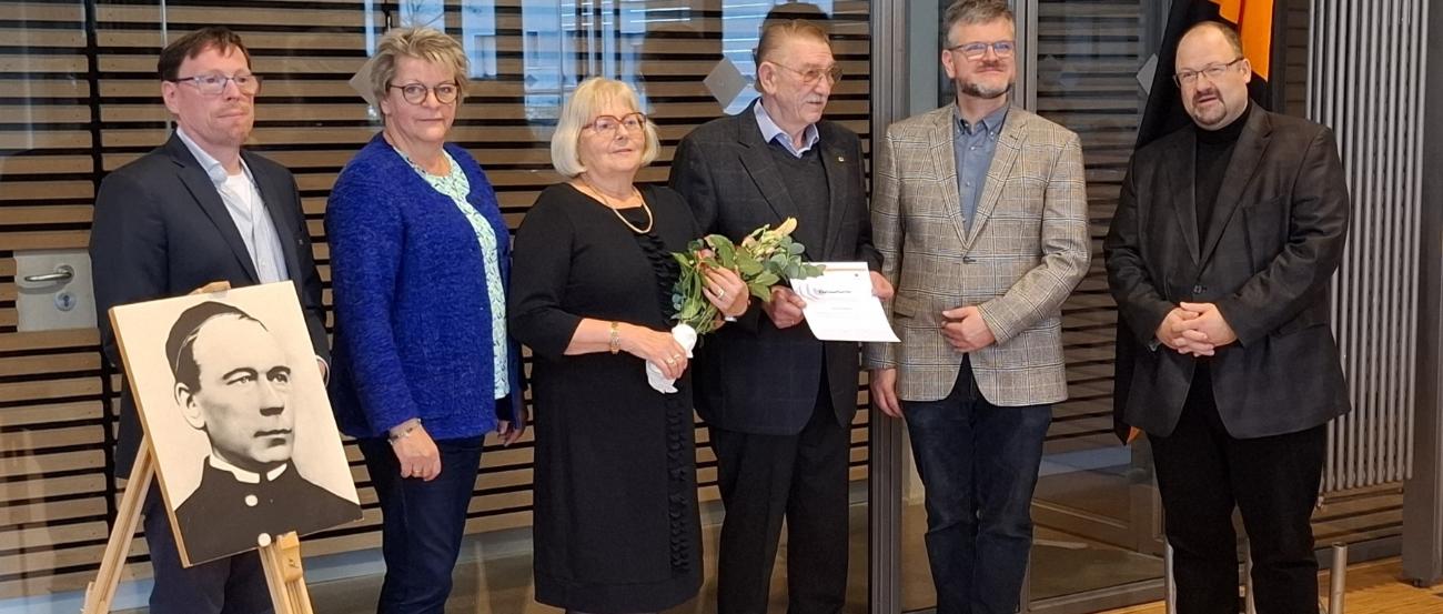 Ehrung des langjährigen Vorsitzenden mit Ehefrau durch das neue Leitungsteam und den Präses, die Personen stehen neben einem Bild von Adolph Kolping.