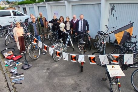 Gruppenfoto, im Hintergrund Garagen, im Vordergrund gesammelte Fahrräder