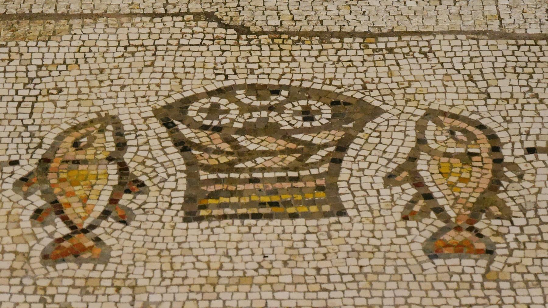 Steinmosaik in Beige- und Brauntönen, das einen Korb mit Broten in der Mitte und an jeder Seite einen Fisch zeigt.